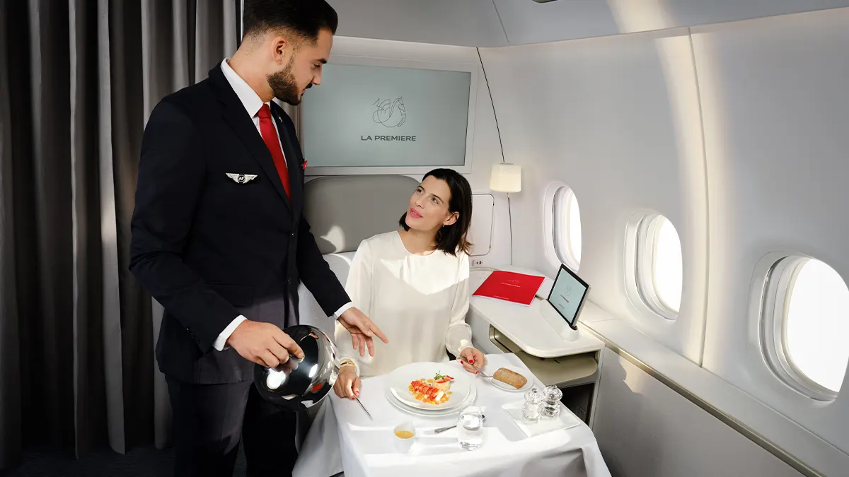 Un membre d’équipage La Première sert un plat à une table dressée dans la suite